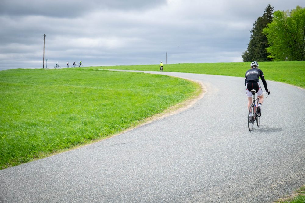 Riders pedal up a hill on a curvy road