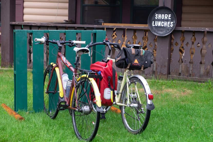 Two bikes parked in front of a restaurant with a sign that reads "Shore Lunches" in the background