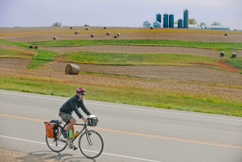 Man riding bicycle on road with farm field and farm in background