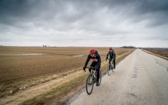 Two cyclists on an empty rural road with gray sky overhead