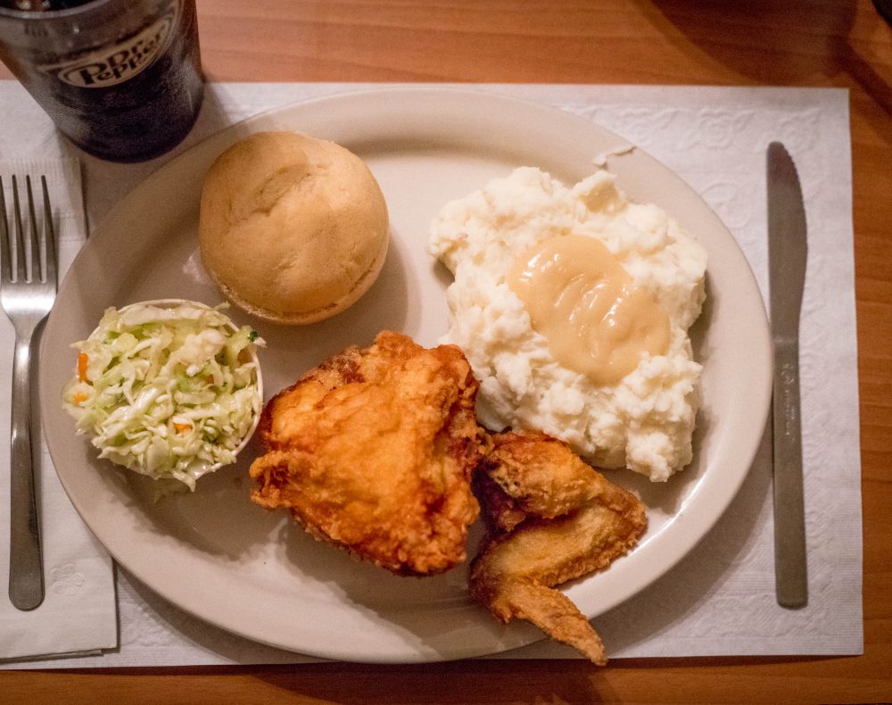 A plate with broasted chicken, mashed potatoes, cole slaw, dinner roll and Dr. Pepper.