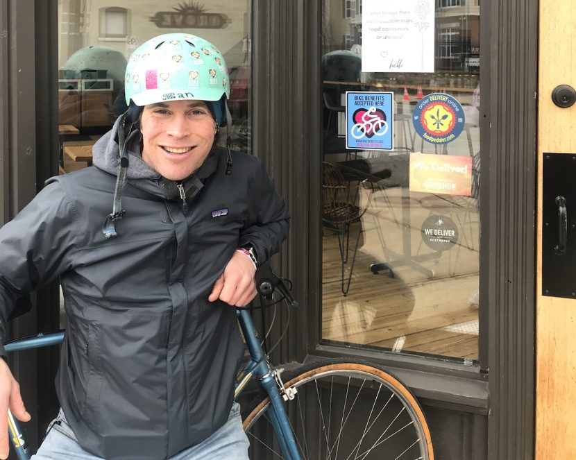 Ian Kepetar with bicycle in front of shop door with Bicycle Benefits sticker on window.