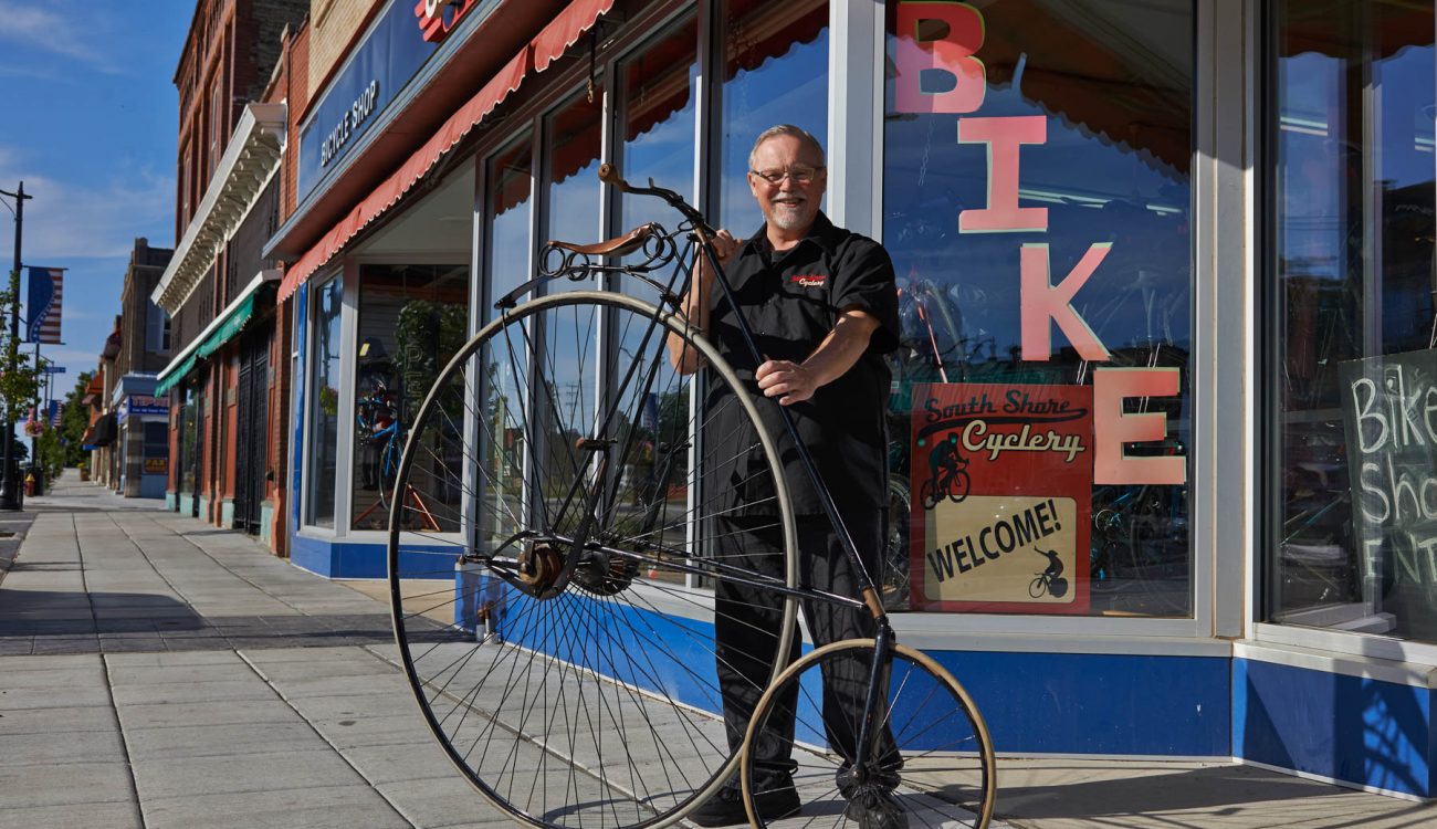 South Shore Cyclery co-owner Scott Nicholes holds an antique penny farthing in front of his shop.