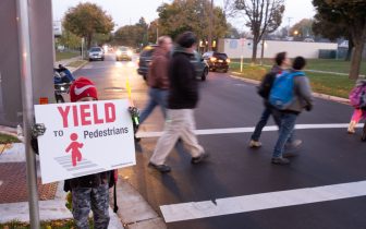 child holds Yield to Pedestrians sign in front of people in crosswalk behind him.