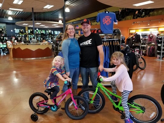 husband and wife with two young girls on bicycles in bike shop