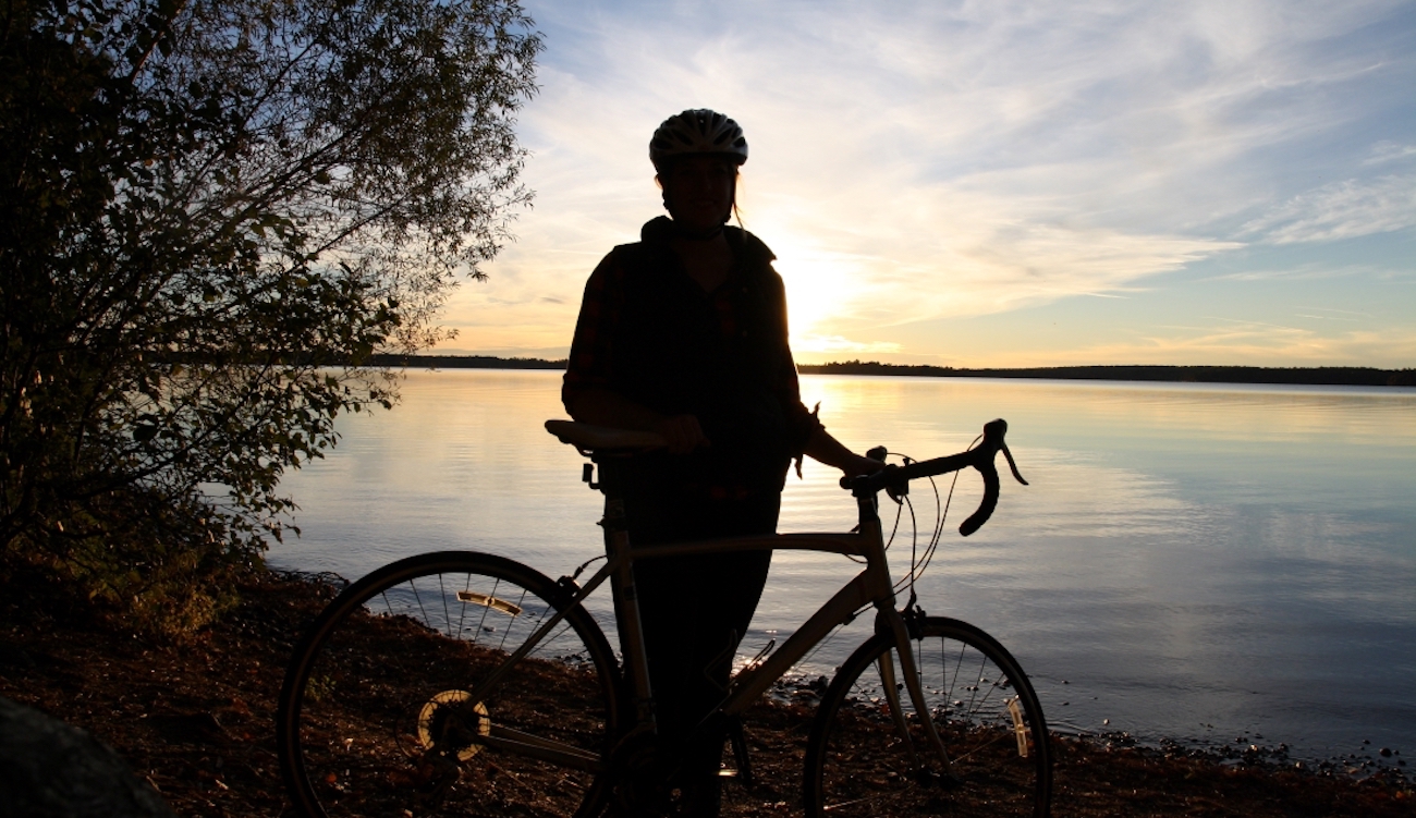woman and bicycle silhouetted against sunset over inland lake