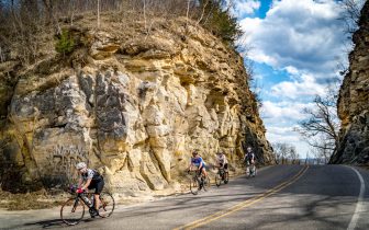 Four cyclists riding through a hand hewn cut in a limestone bluff
