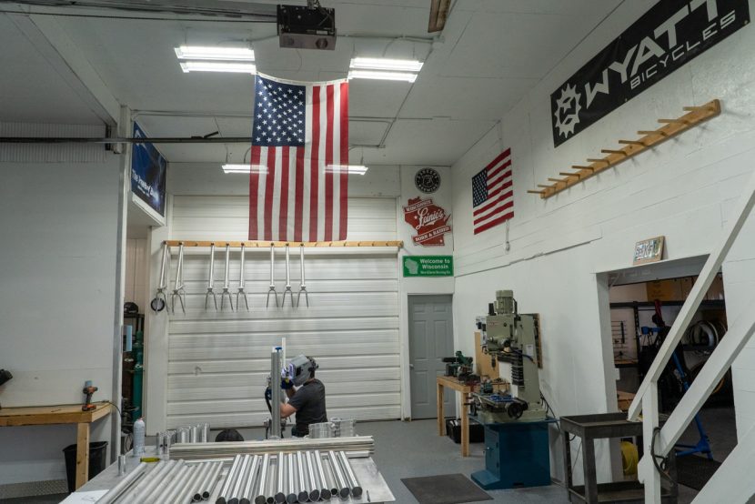 A man welds inside a shop with an american flag and Wyatt Bicycle banner