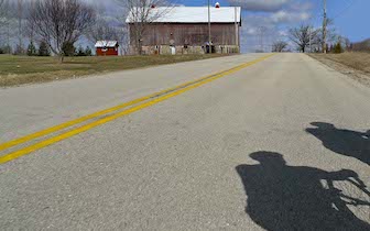 Shadow of riders on paved rural road with red barn in distance