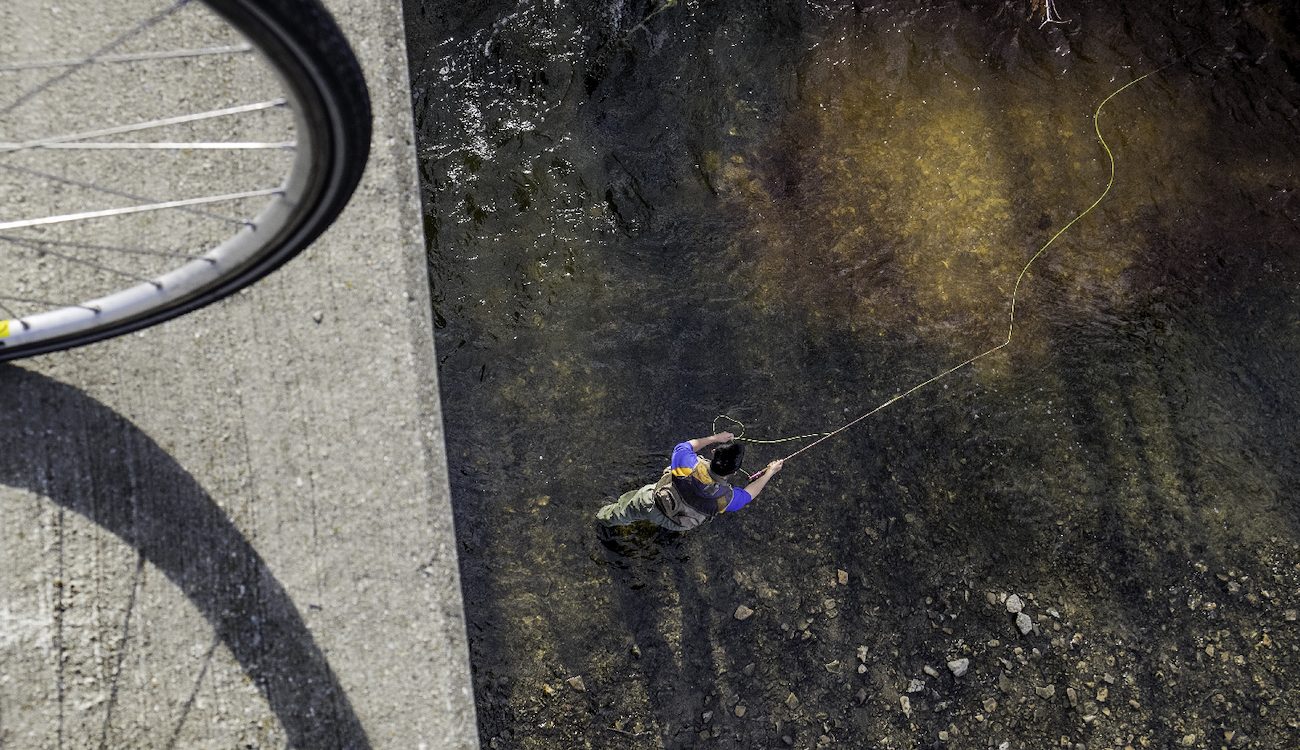bicycle tire on bridge over man fly fishing in river below