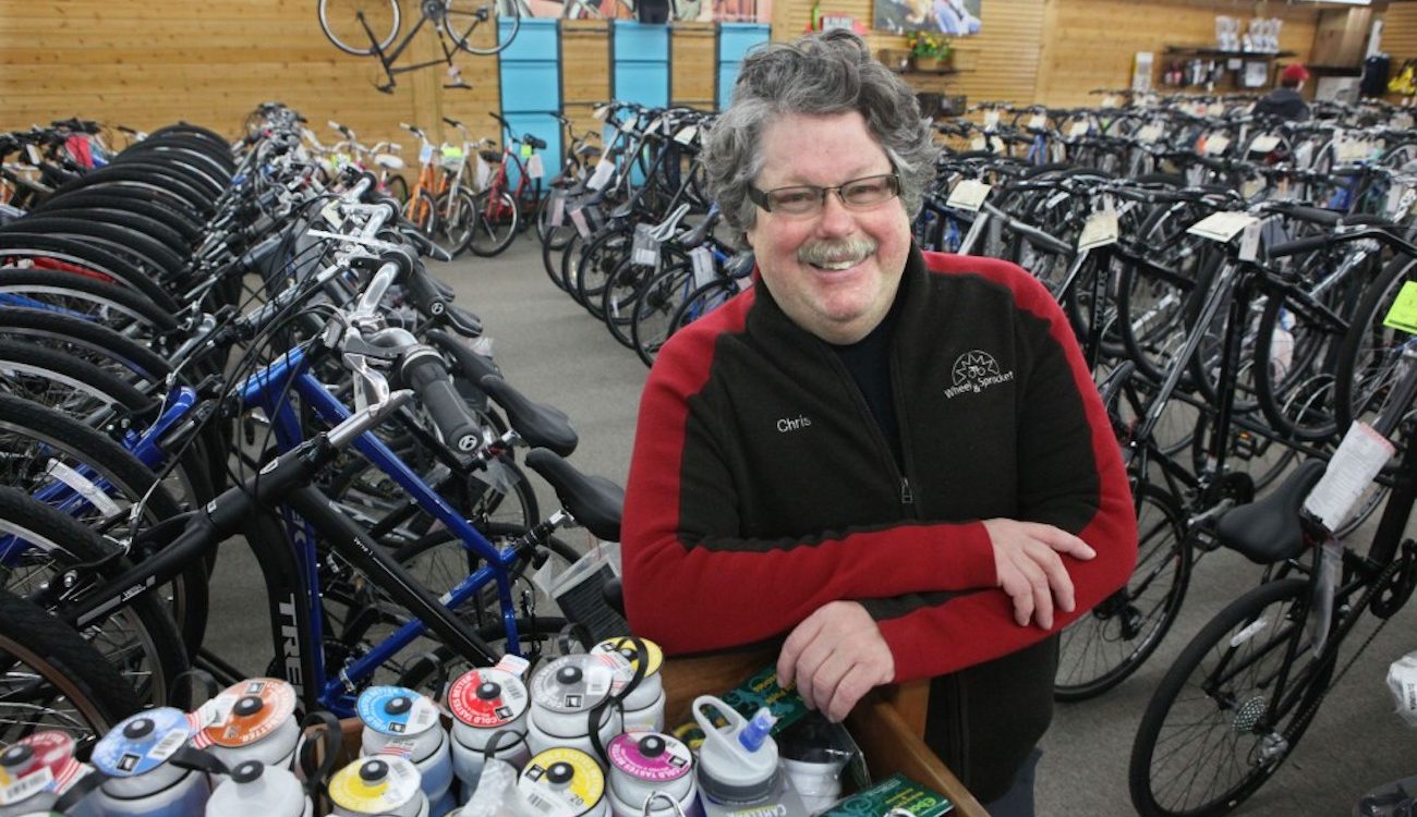Chris Kegel leans on waterbottles with bikes behind him in the Hales Corners Wheel and Sprocket Store