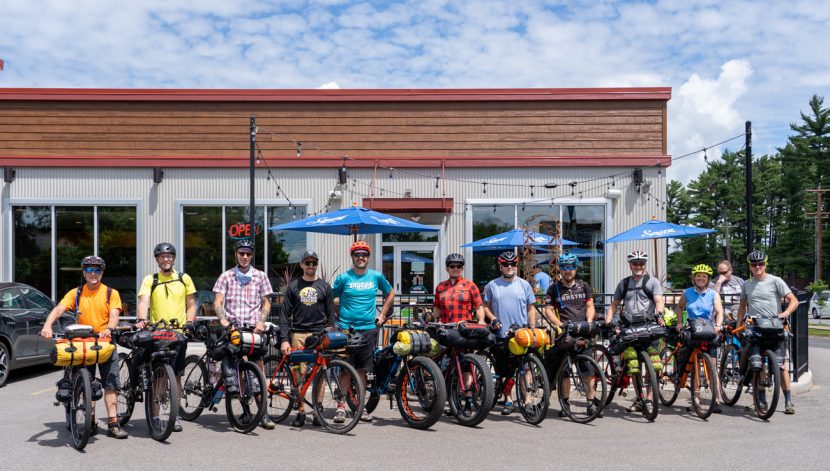 11 people pose next to bicycles outside a restaurant