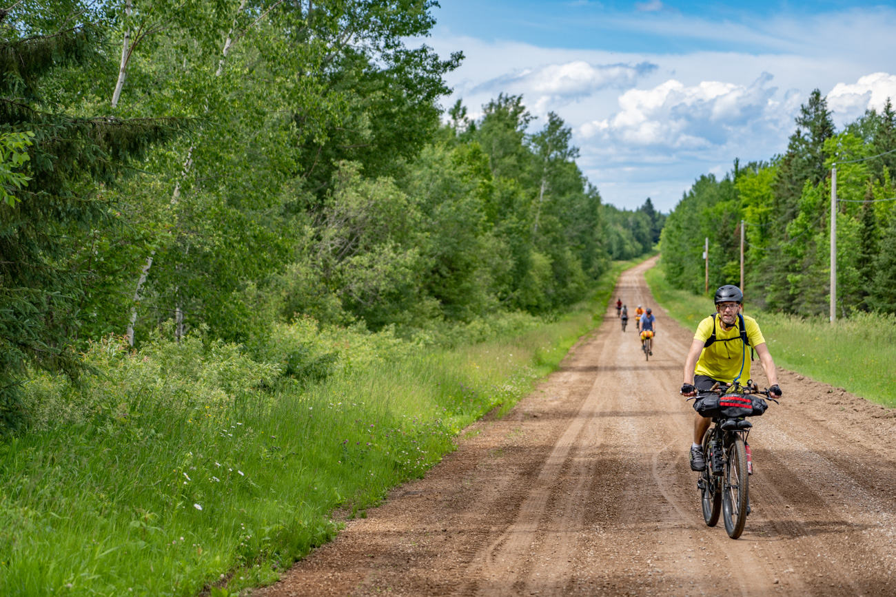 people on bicycles ride a gravel road at the camera