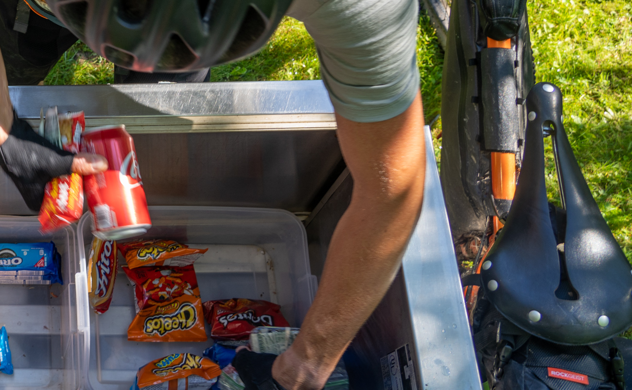 reaching into cooler for soda and snacks with bike leaning on cooler