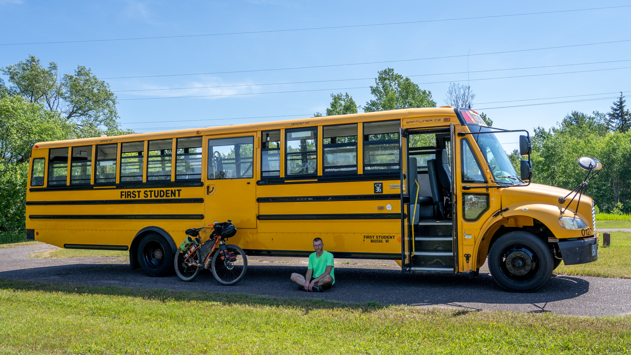 Man sits next to bicycle and school bus