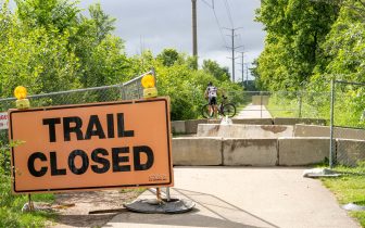 A person on a bicycle walks over concrete barriers past a trail closed sign