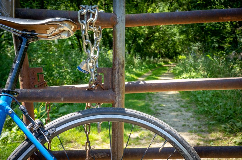 bicycle leans against a gate closed with a chain and padlock.