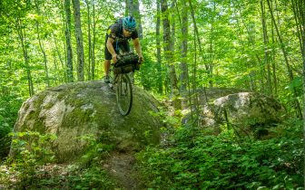 Man rides bike down big boulder in forest