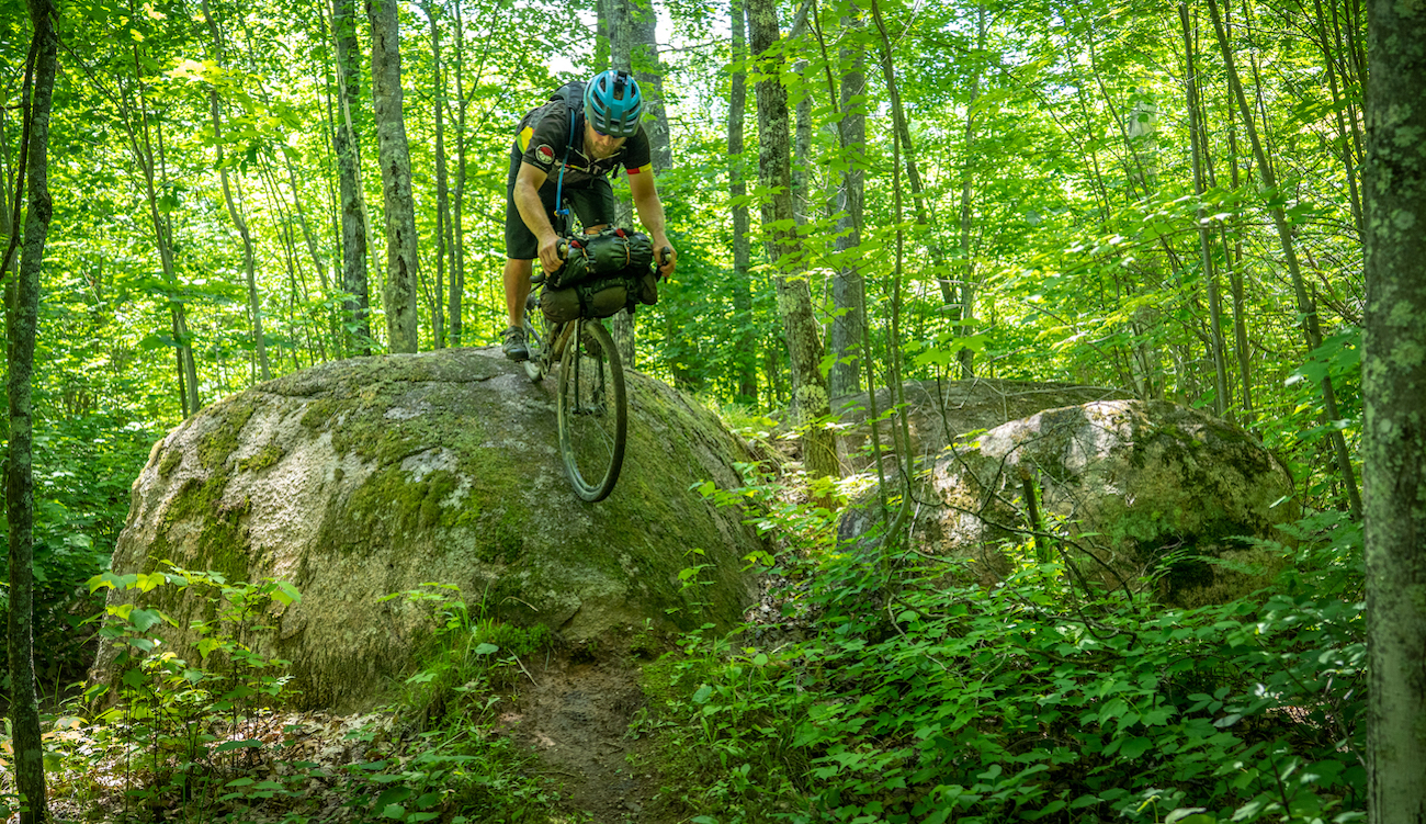 Man rides bike down big boulder in forest