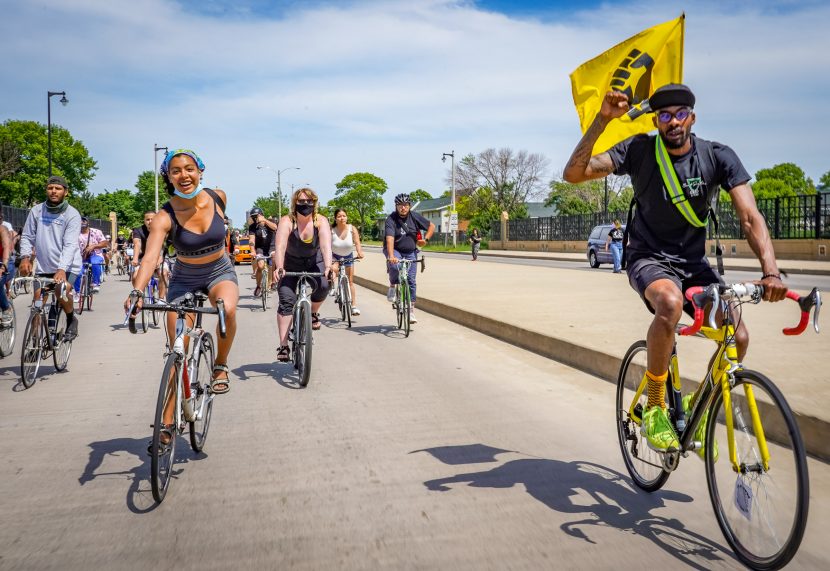 A man on a bicycle with a black power flag rides toward the camera during the black is beautiful ride.