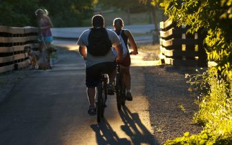 backlit photo of two kids riding bikes on trail and woman with dog on leash