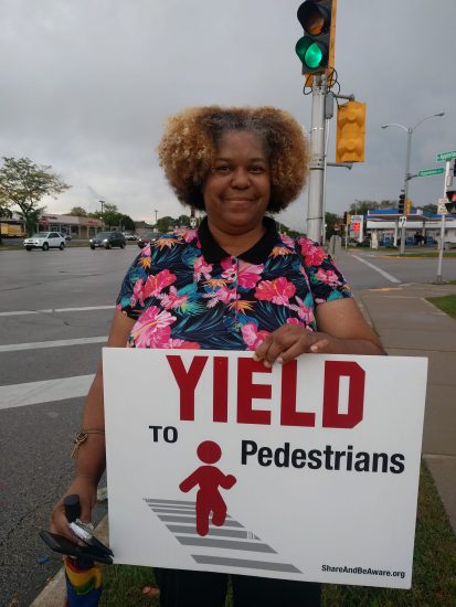a woman folds a yard sign up at a street intersection asking people to yield