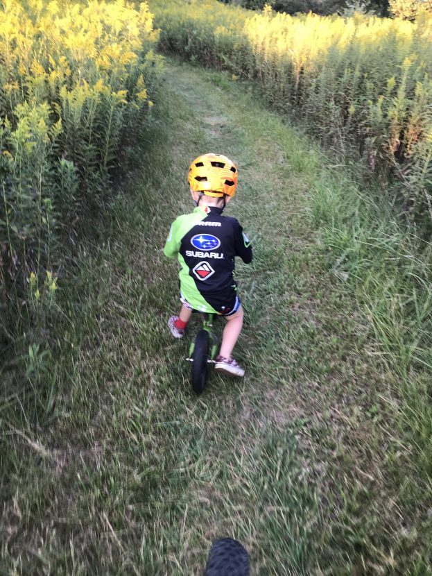 young child rides a pedal less bike on grassy trail