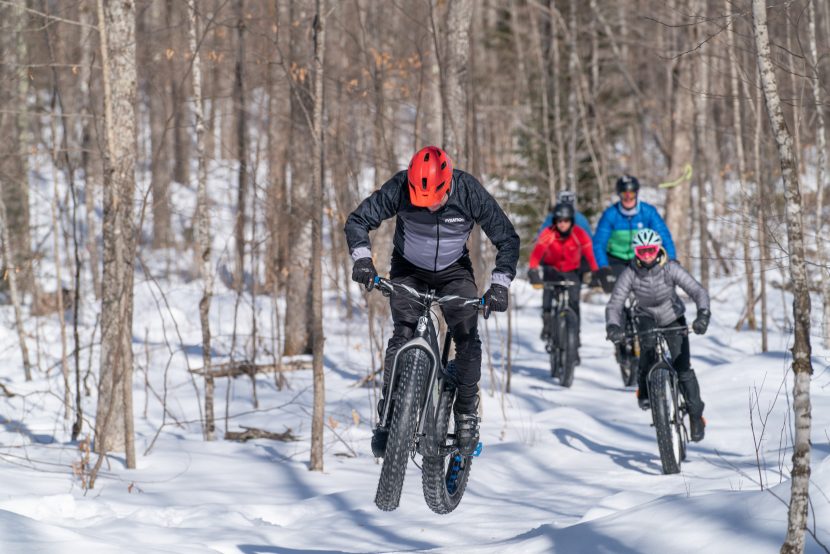 A man on a fat bike gets some air on a snowy trail.