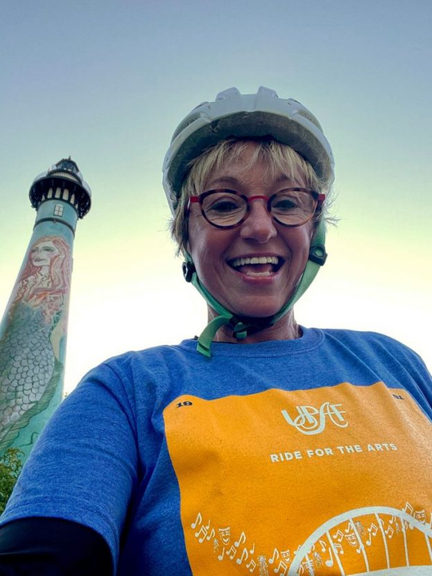 A cyclist takes a selfie with a lighthouse in the background.