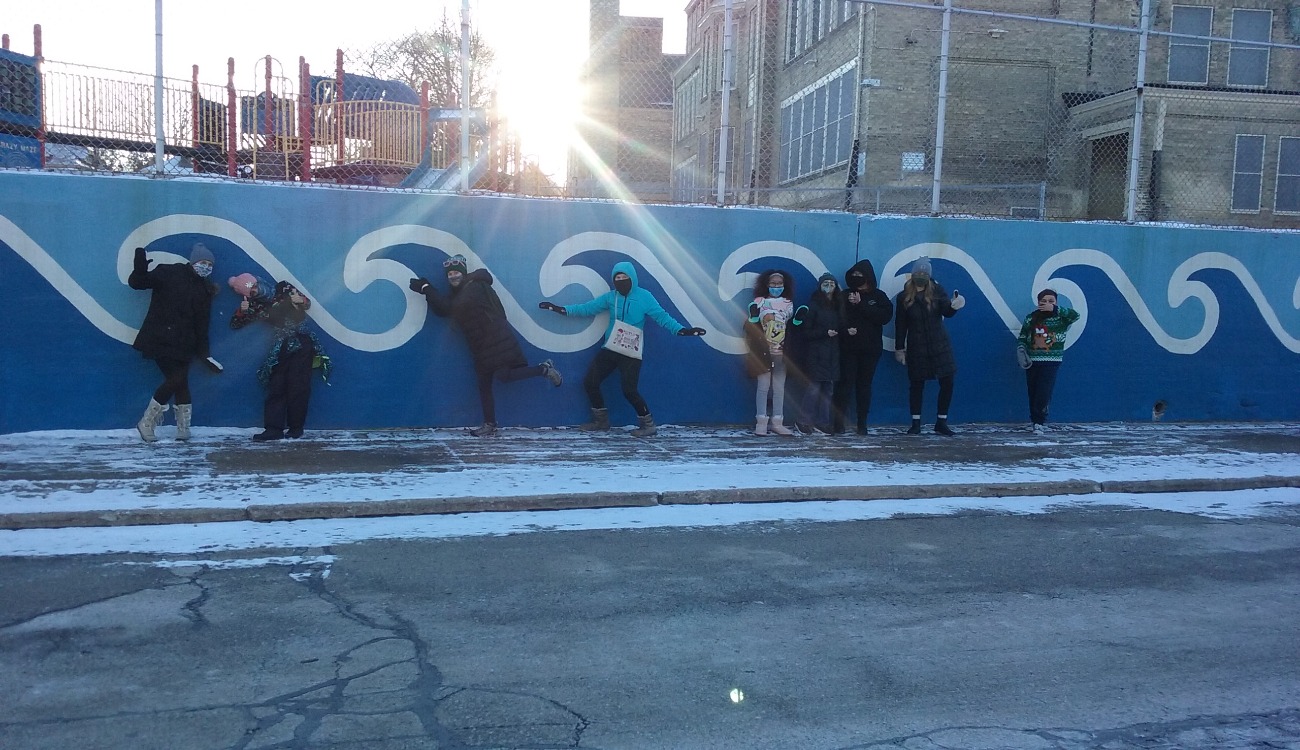 kids in winter clothing stand next to a wave mural