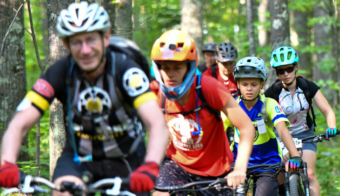 Coach riding bicycles with kids through woods