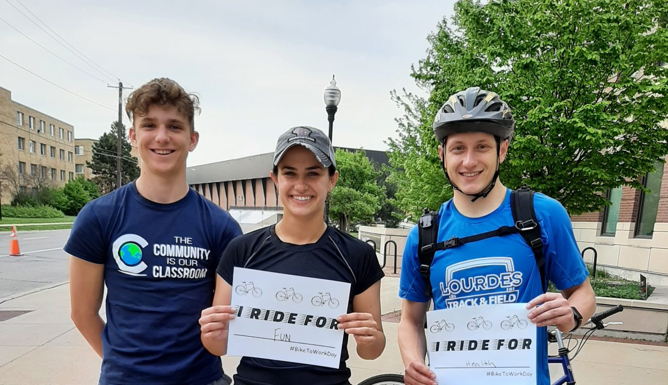 Three student cyclists posing with signs about why they bike