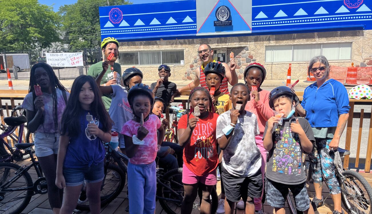 children and adult instructor eating popsicles on a hot day at a outdoor dining parklet after riding their bikes there