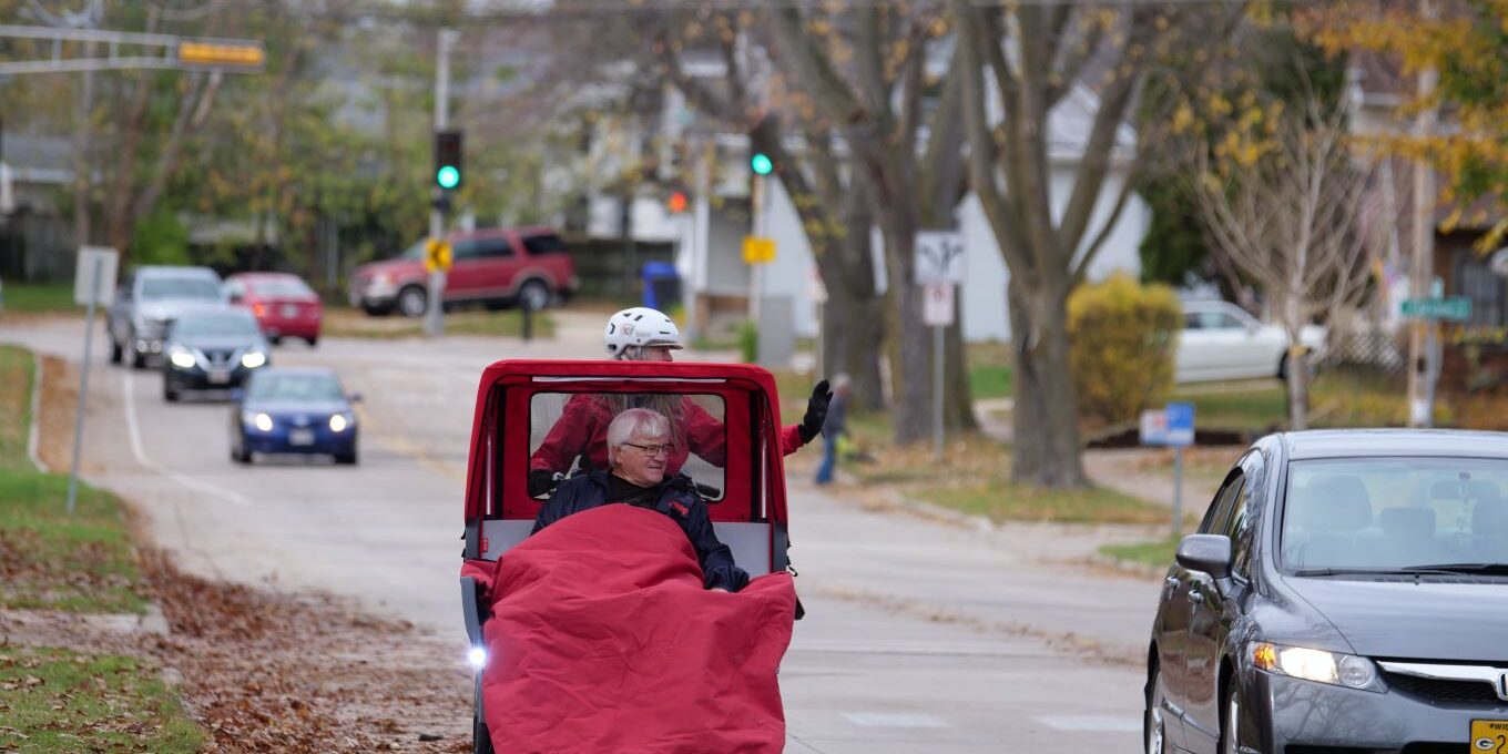 Cycling Without Age pilot pedals a passenger down the street in a trishaw