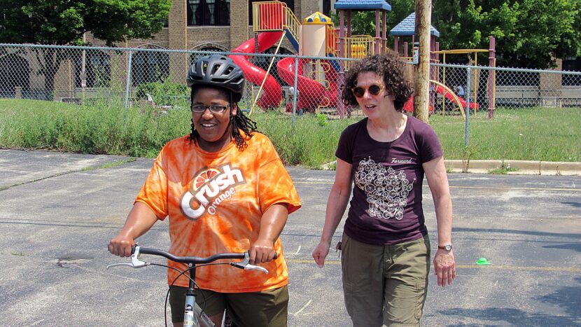 woman in orange shirt learns to use a balance bike with another woman safety instructor 