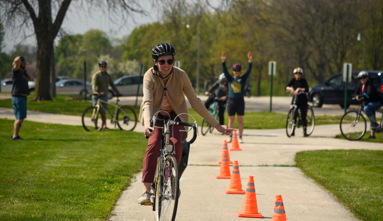 Adult bike rider weaves around safety cones while learning skills by instructor behind them