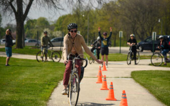 Adult bike rider weaves around safety cones while learning skills by instructor behind them