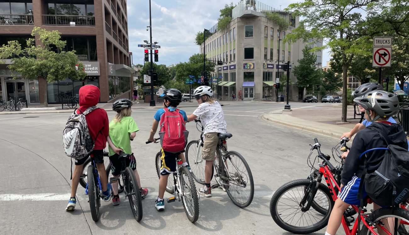 5 kids on bikes wait at an intersection in downtown Madison