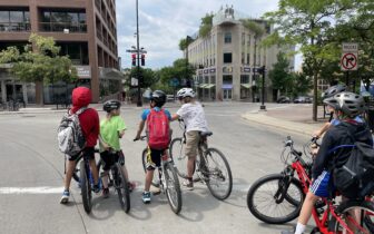 5 kids on bikes wait at an intersection in downtown Madison