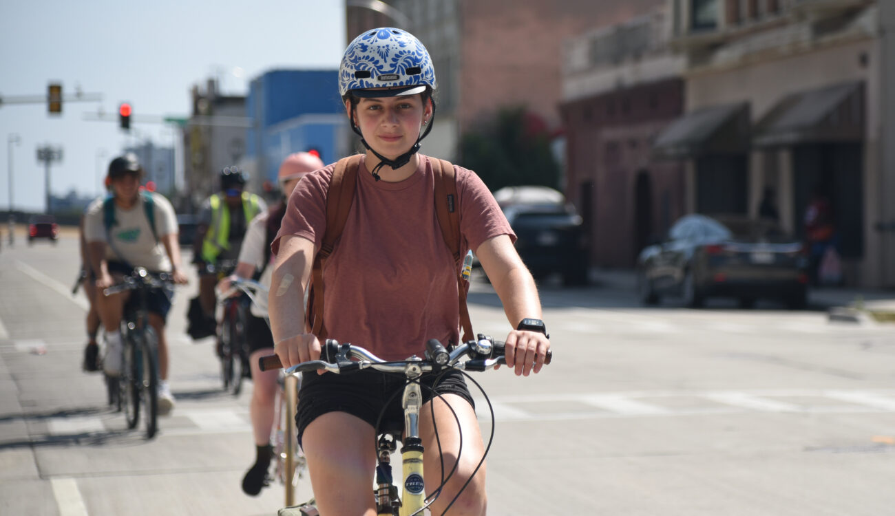 A group of teens bike along a bike lane on a road toward the camera