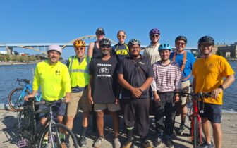 a group of people stand next to the rider and under the hoan bridge smiling and posing for the photo