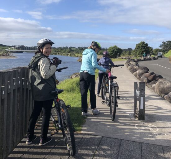 Three women with bikes on a path near a river