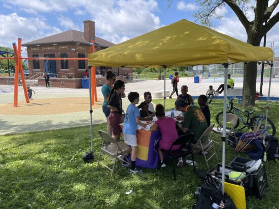 A group of adults and children under a yellow canopy at a playground